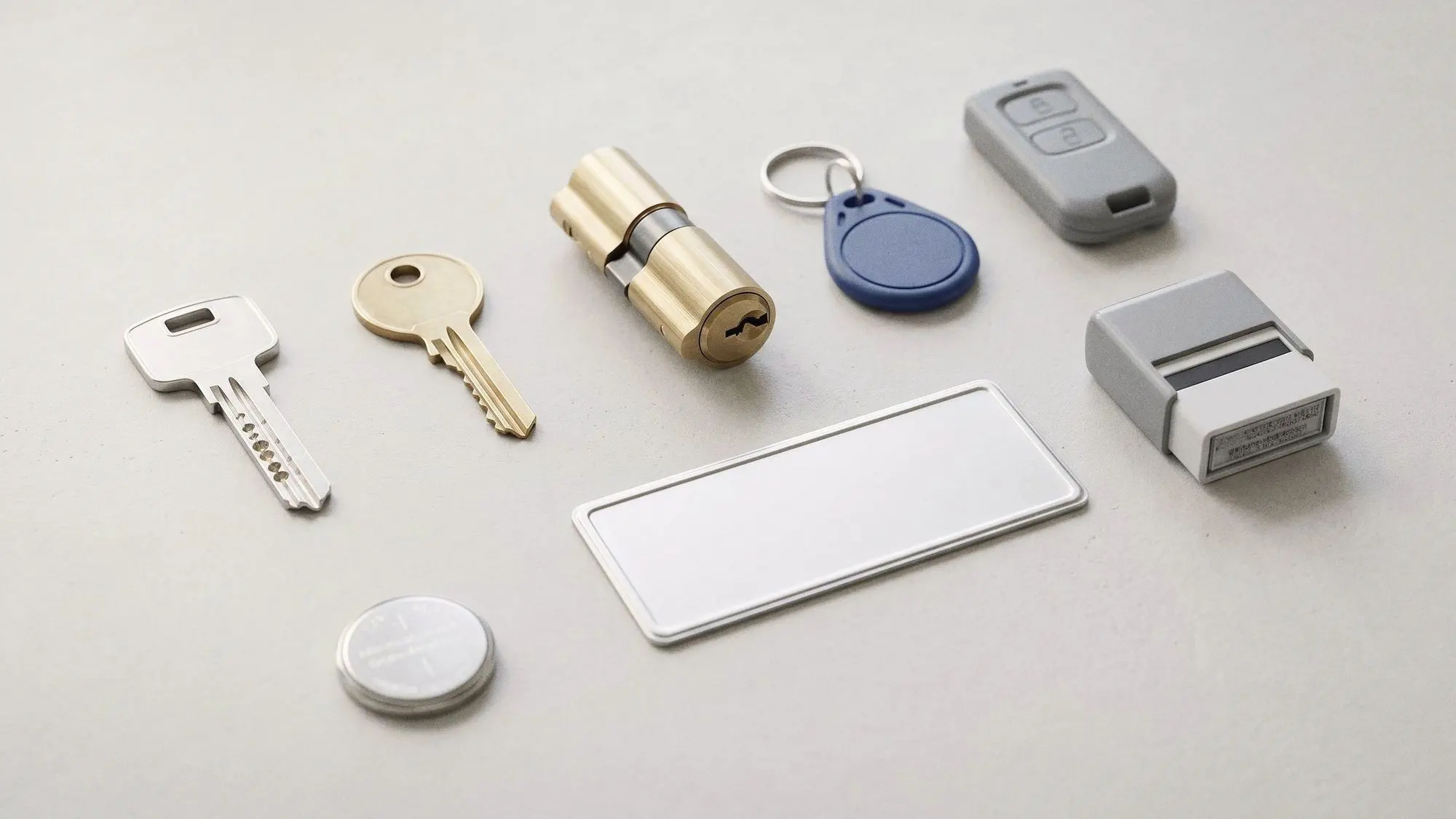 Clé de sécurité, cylindre, badge, télécommande, plaque et tampon alignés sur un plan clair
